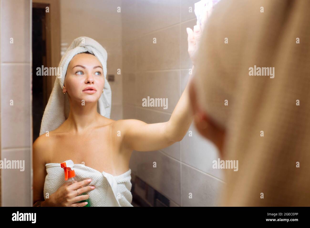 Cleaning in the shower room. A beautiful girl washes the mirror with a rag Stock Photo