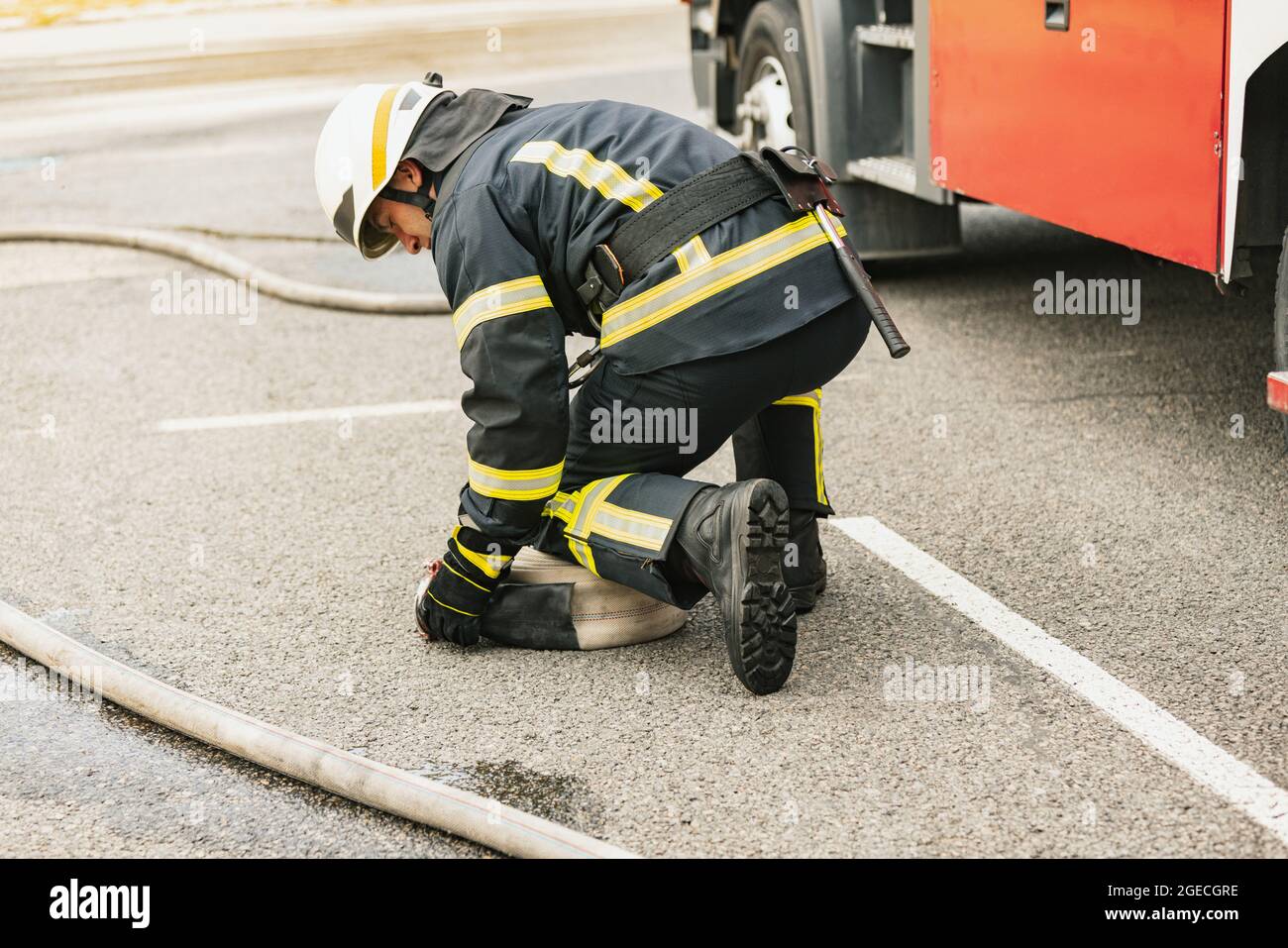 One young male firefighter dressed in uniform with water hose at fire ...