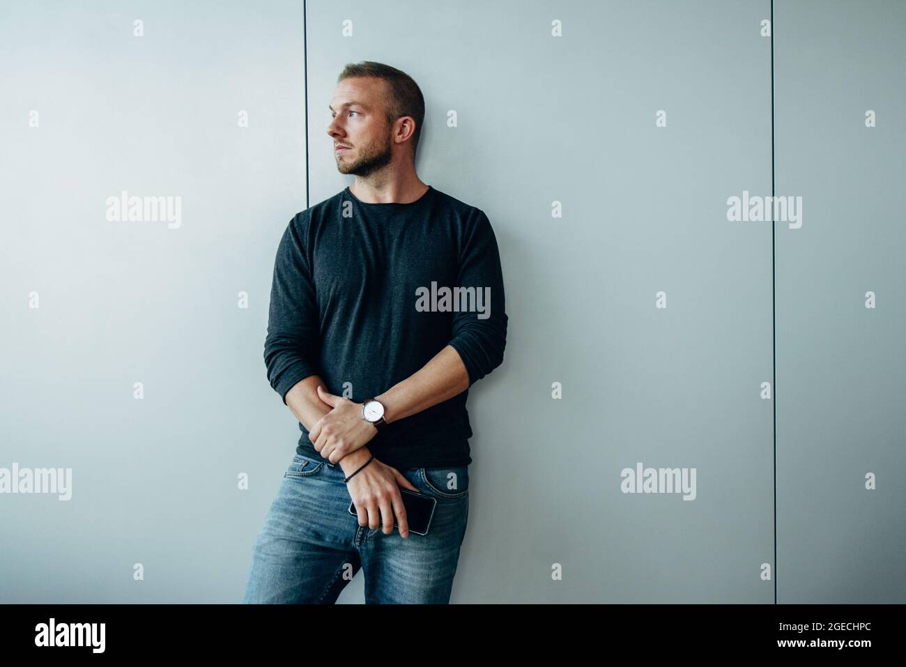 Young man leaning to a wall and looking away. Thoughtful male professional in office. Stock Photo