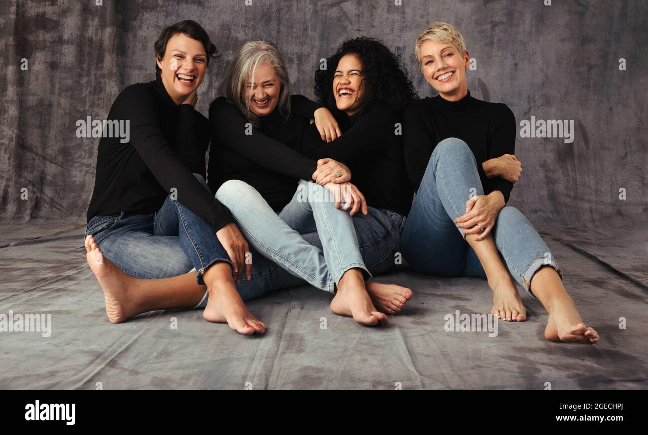 Fashionable women of different ages celebrating their natural and aging bodies. Four body positive women laughing together while wearing jeans and sit Stock Photo