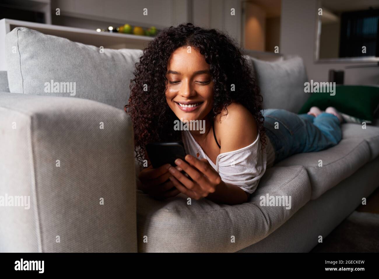 Mixed race female student relaxing on couch texting on cellular device Stock Photo