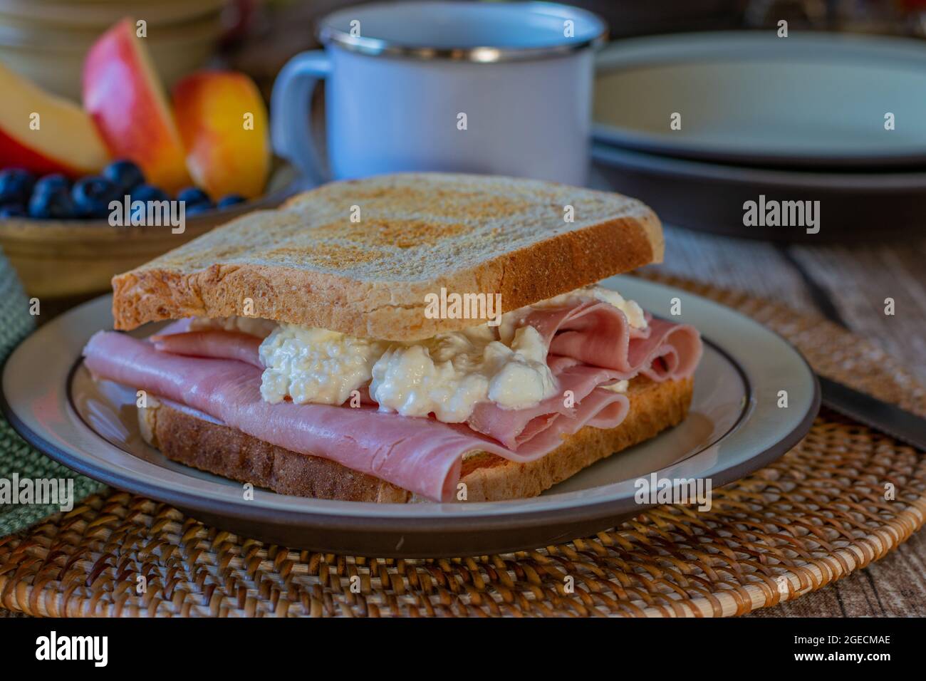 Toasted Breakfast sandwich with whole wheat toast,  thin sliced ham and cottage cheese. Served with a cup of coffee and a bowl of fruits Stock Photo