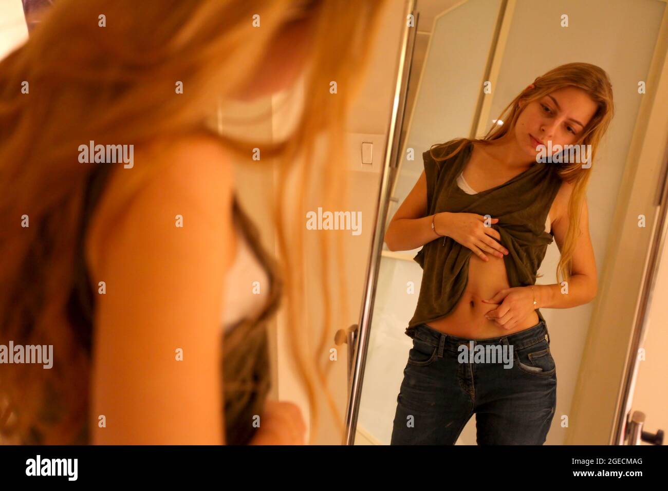 Young Woman pinching her waist. She may be keeping track of weight loss during a diet but compulsive body analysis may be a symptom of a body image di Stock Photo