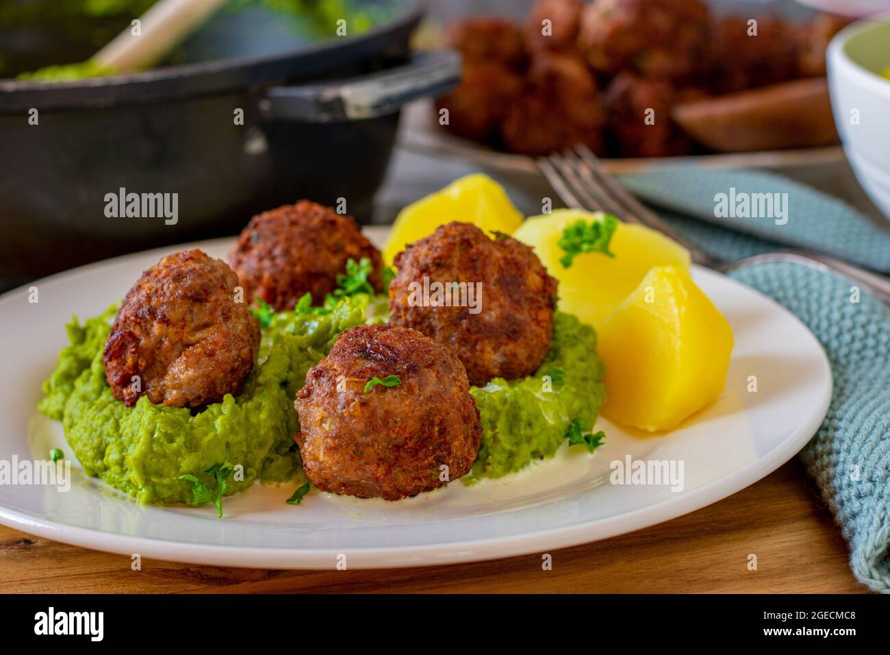 Fried meatballs with pea puree and potatoes on a plate with kitchen table background. Stock Photo