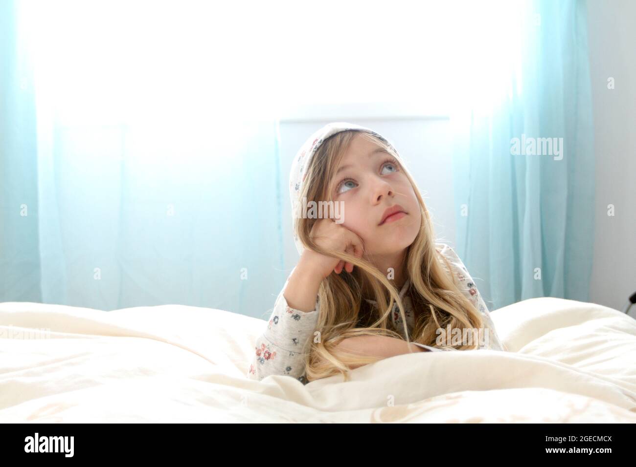 Young girl of seven daydreams in her bedroom Stock Photo