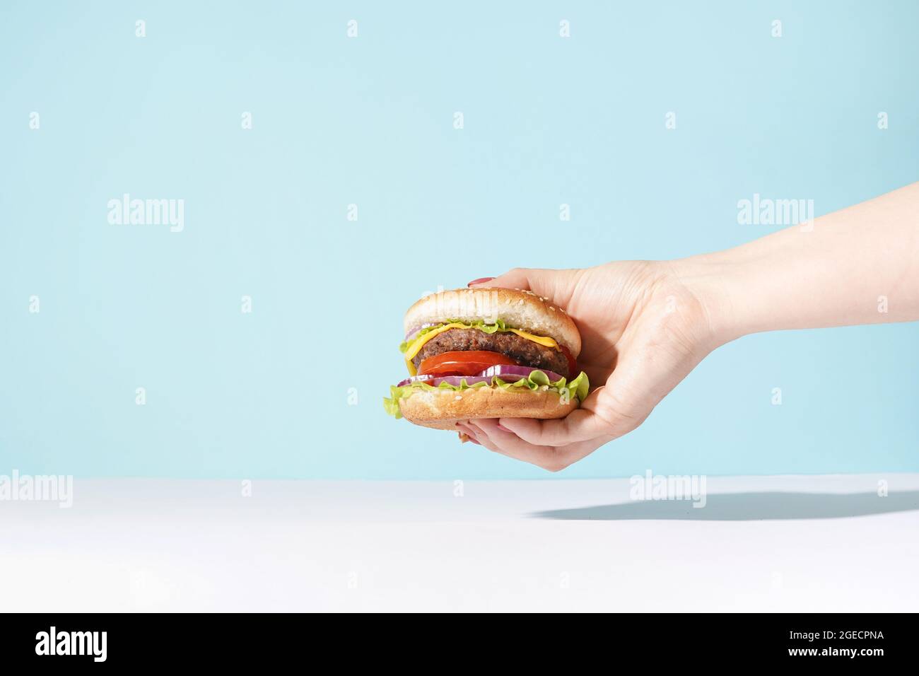 Hand holding a burger on blue background. eating and healthy concept, copy space Stock Photo