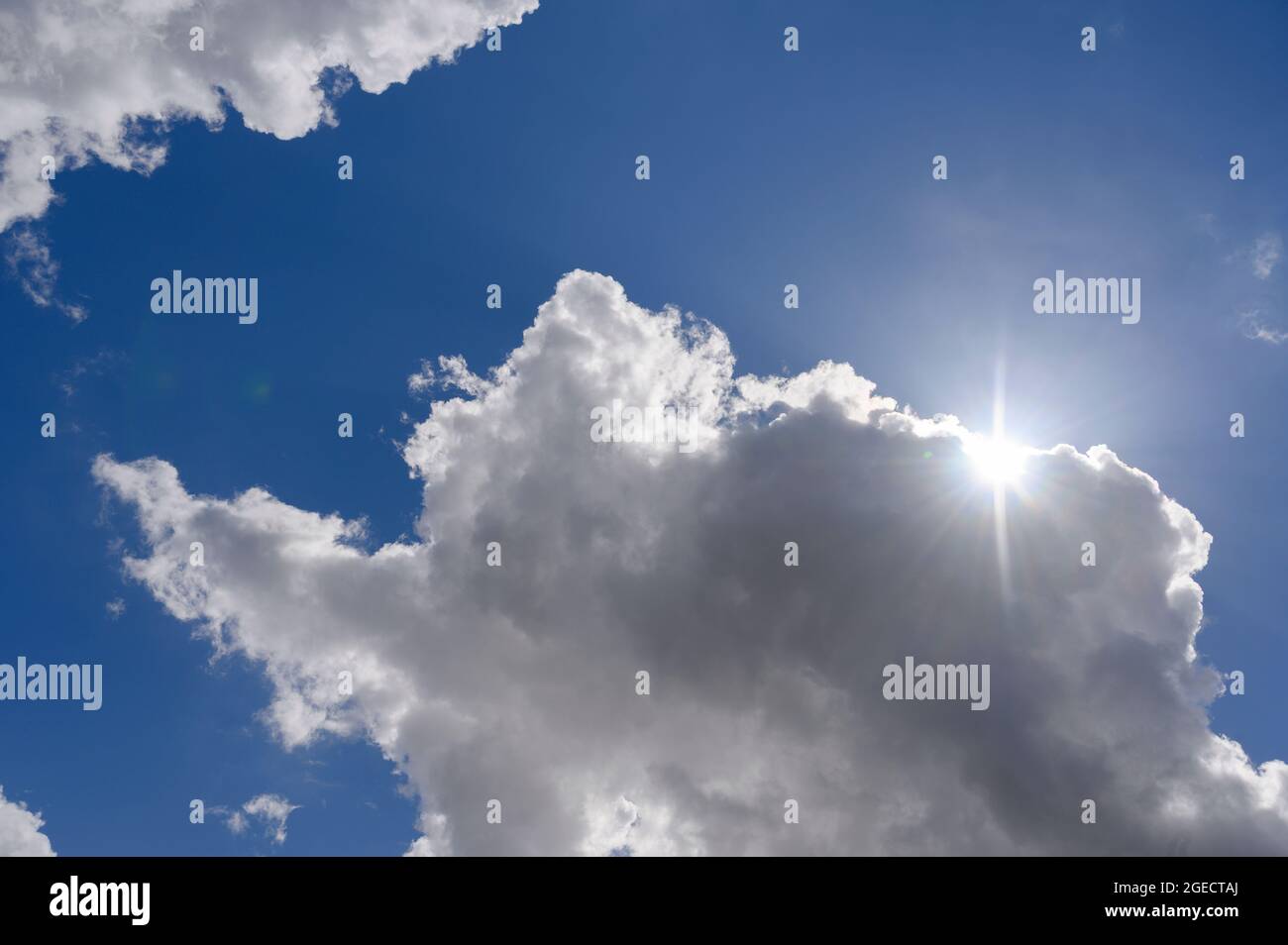 Fluffy white clouds passing in front of the sun in a bright blue sky. Stock Photo