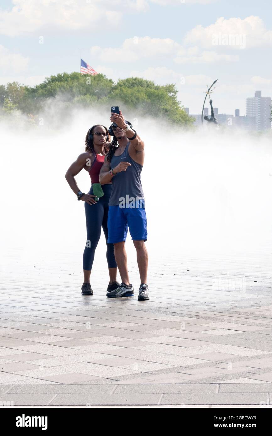 A very fit couple take selfies at the Fountain of the Fairs in Flushing Meadows Corona Park in Queens, New York City. Stock Photo