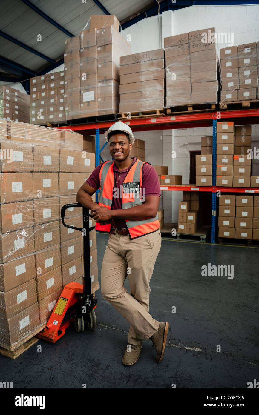 Mixed race male worker standing besides parcels smiling in warehouse  Stock Photo