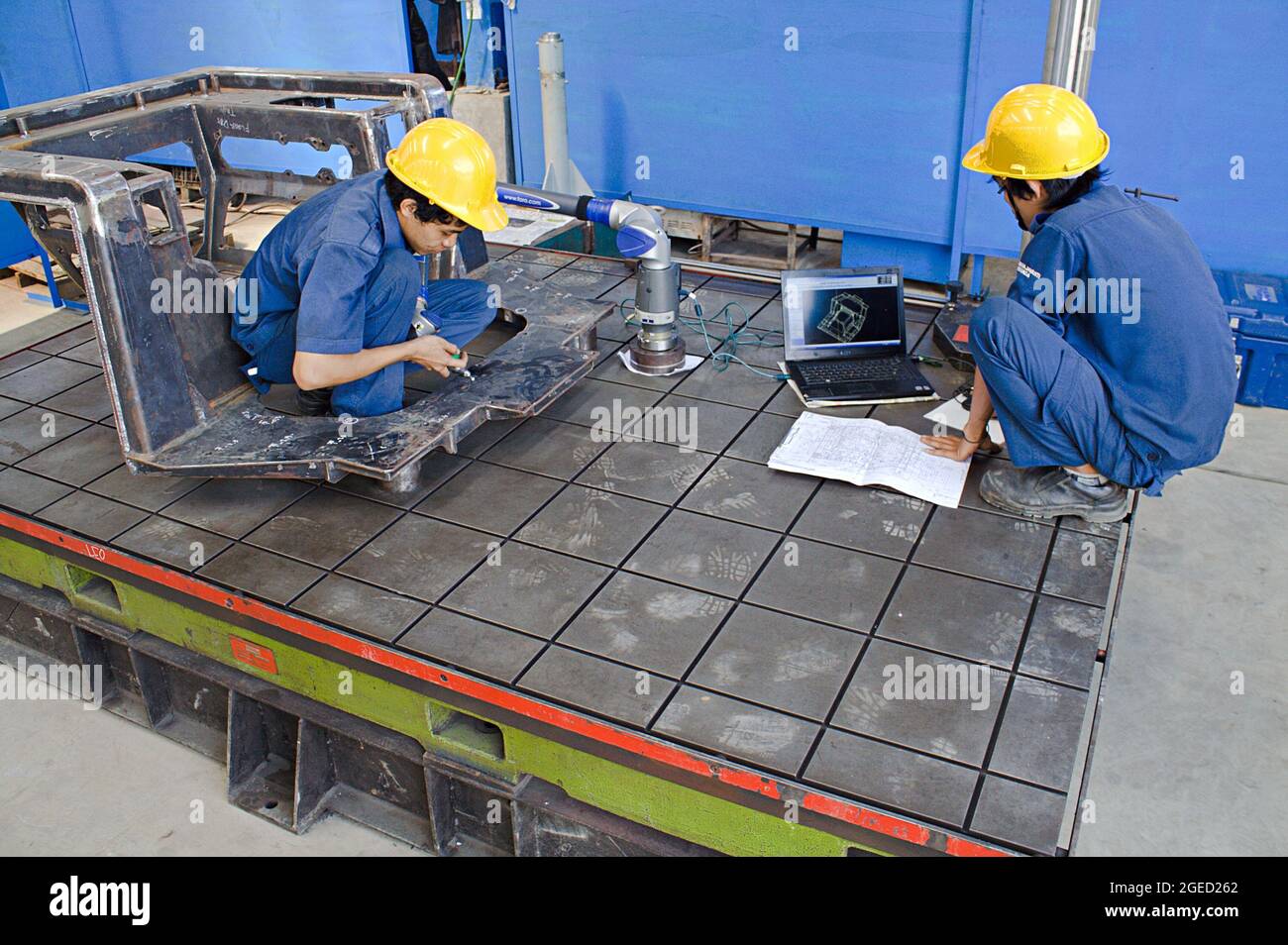 Two technicians use measurement tool and laptop in a metal fabrication