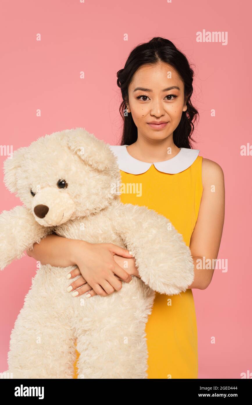 happy asian young woman in yellow dress holding teddy bear isolated on