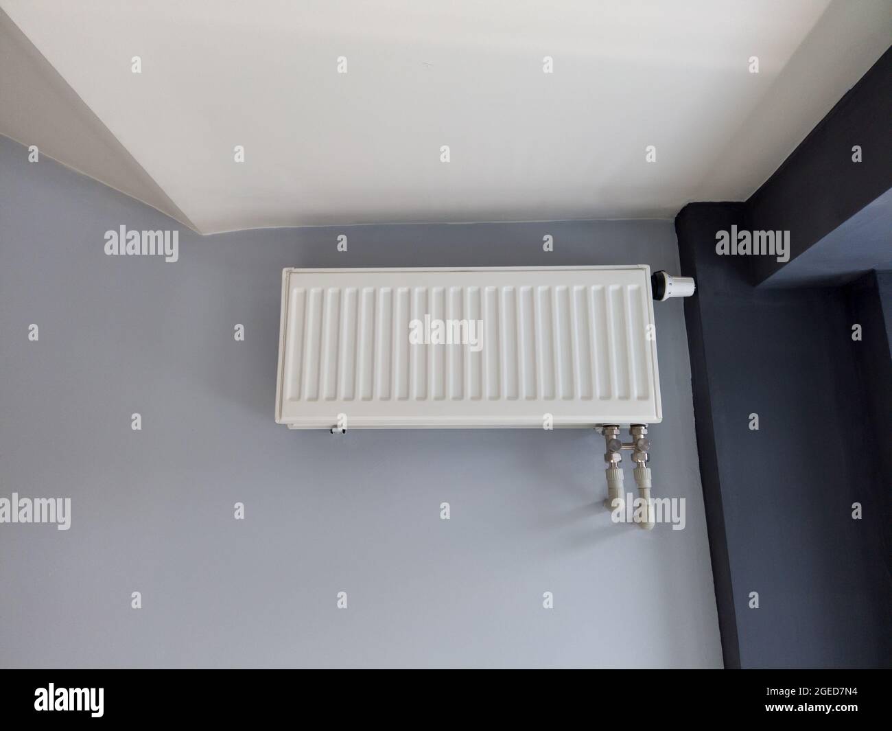 White heating radiator with thermostat on gray wall. Modern plastic