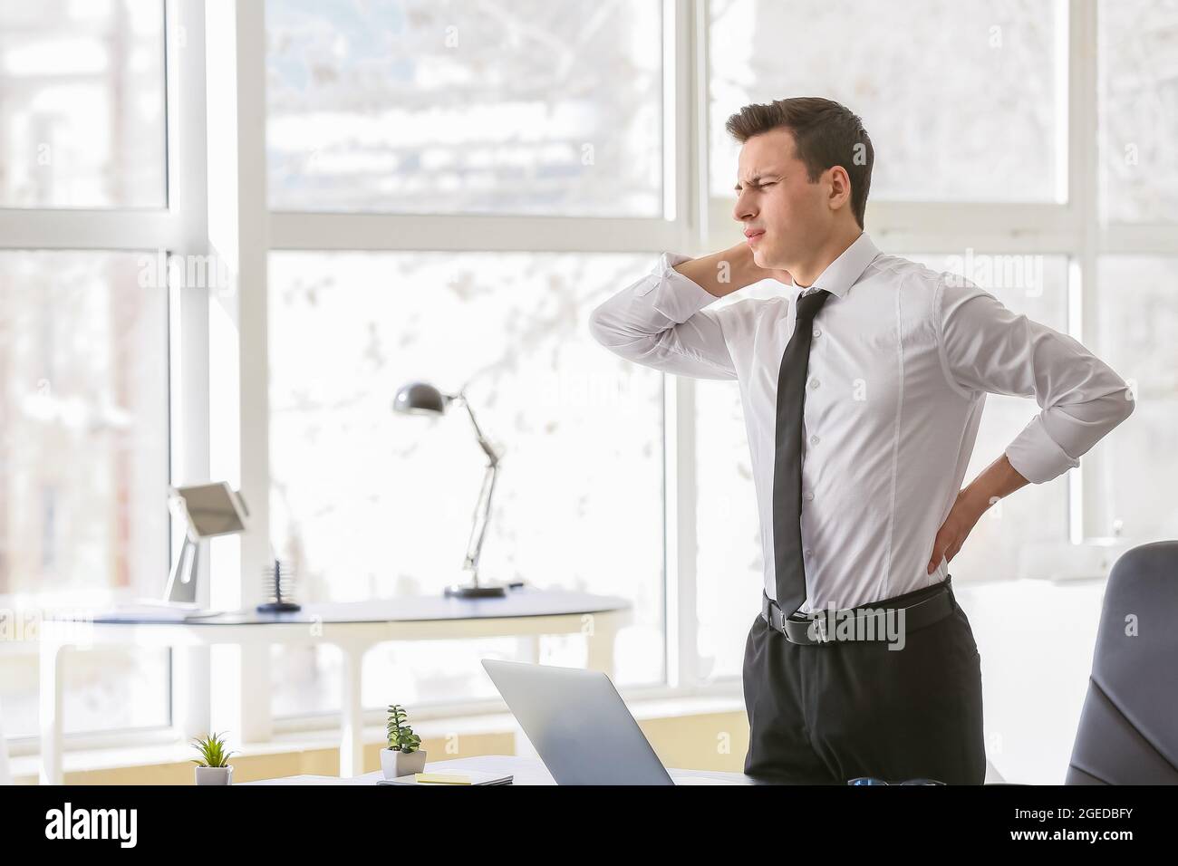 Young man suffering from back pain in office Stock Photo - Alamy