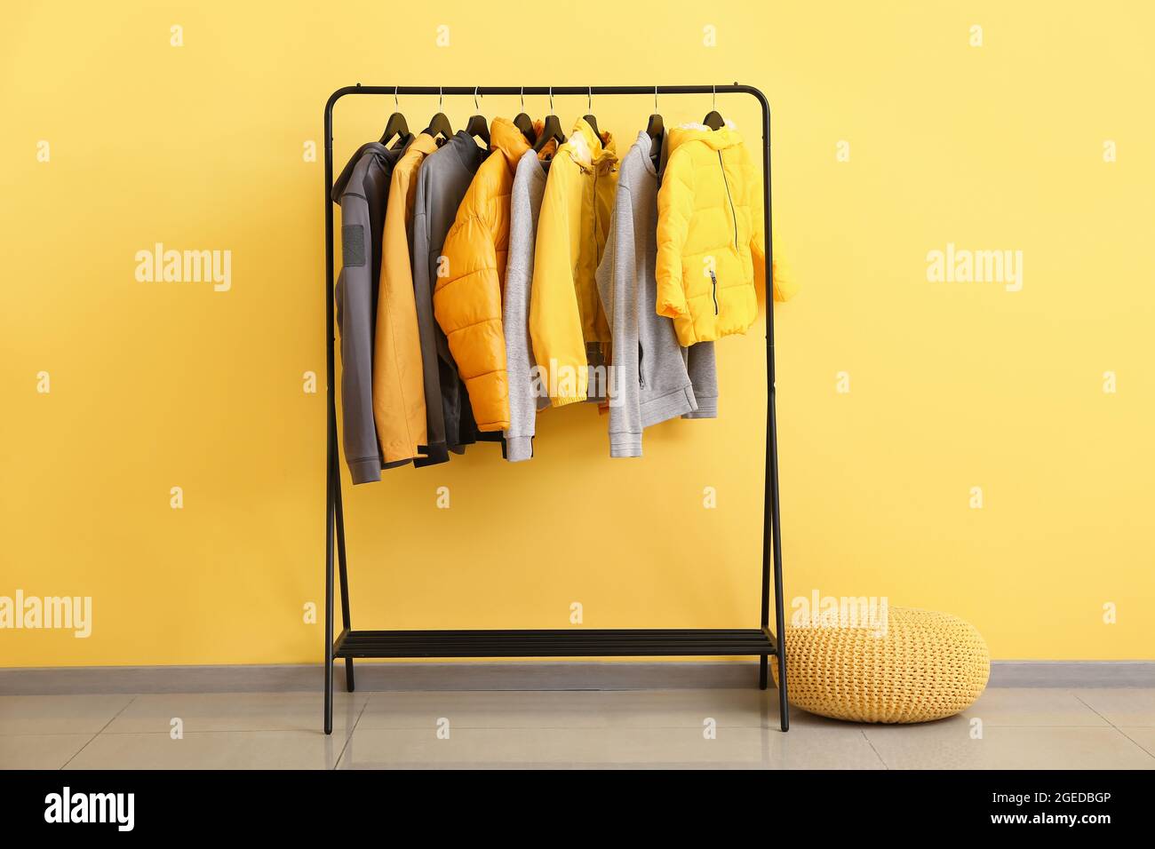 Rack with stylish clothes and pouf near color wall Stock Photo