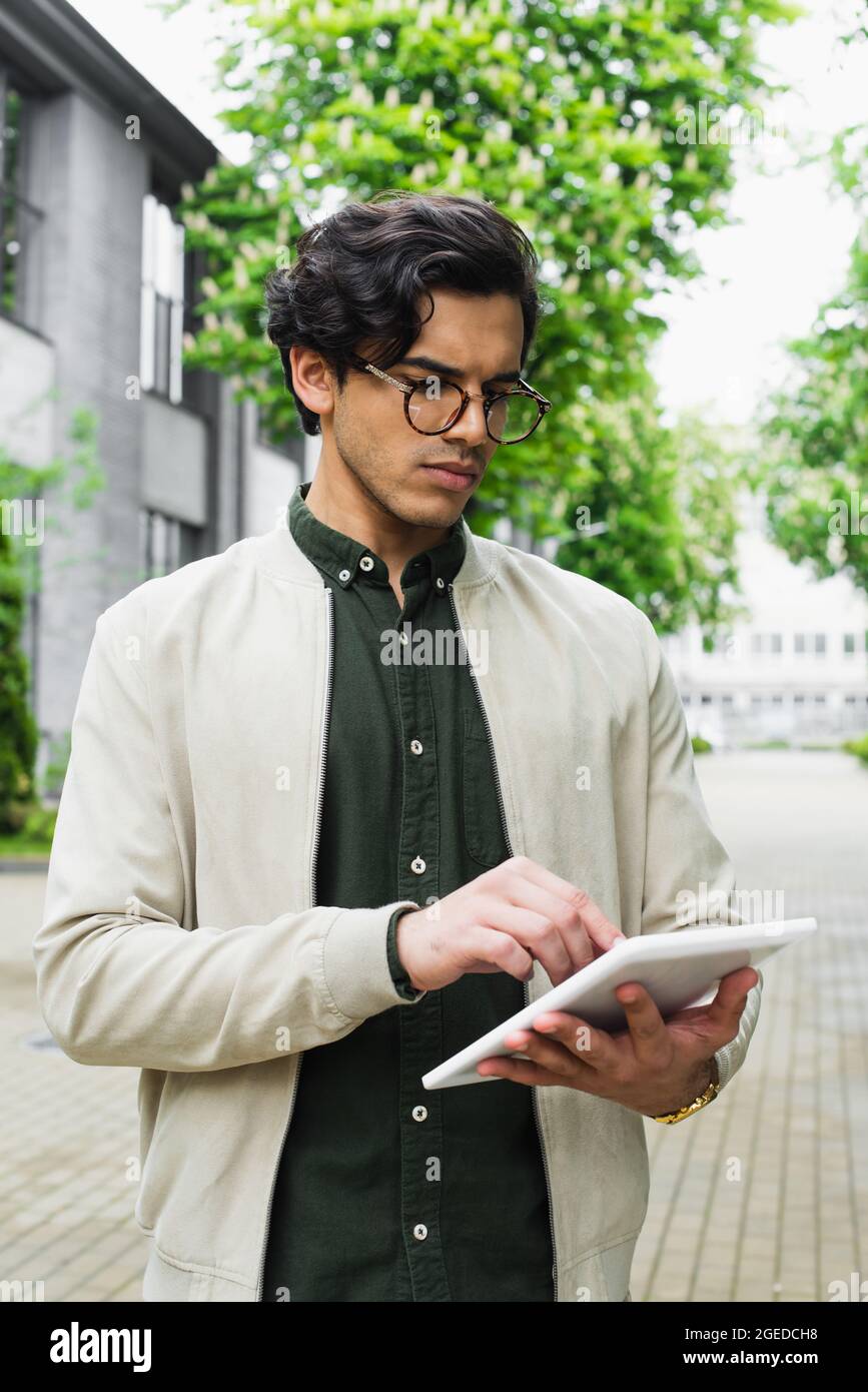 young man in eyeglasses and bomber jacket using digital tablet outside  Stock Photo - Alamy
