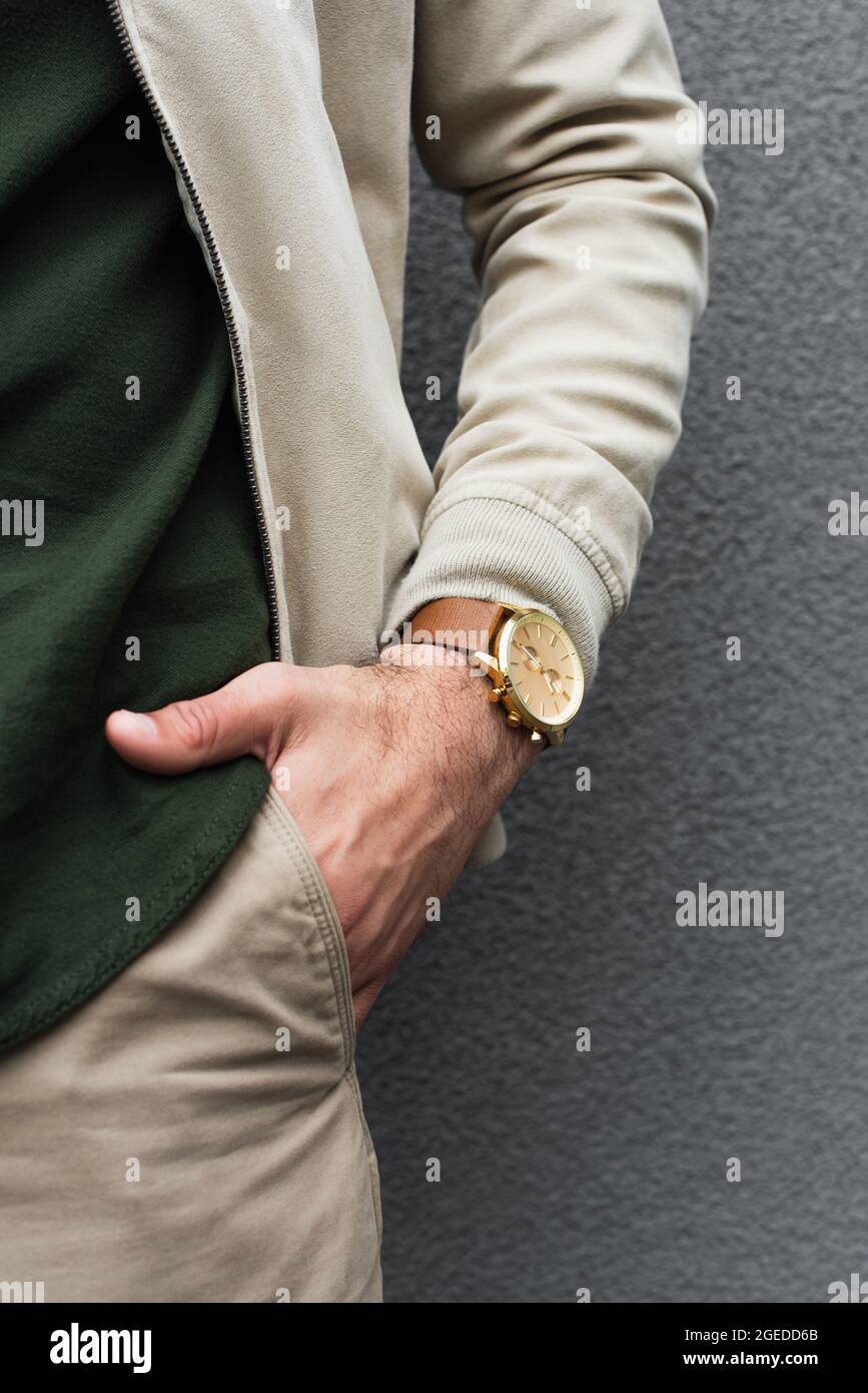 cropped view of young man with stylish wristwatch posing with hand in pocket near grey wall Stock Photo