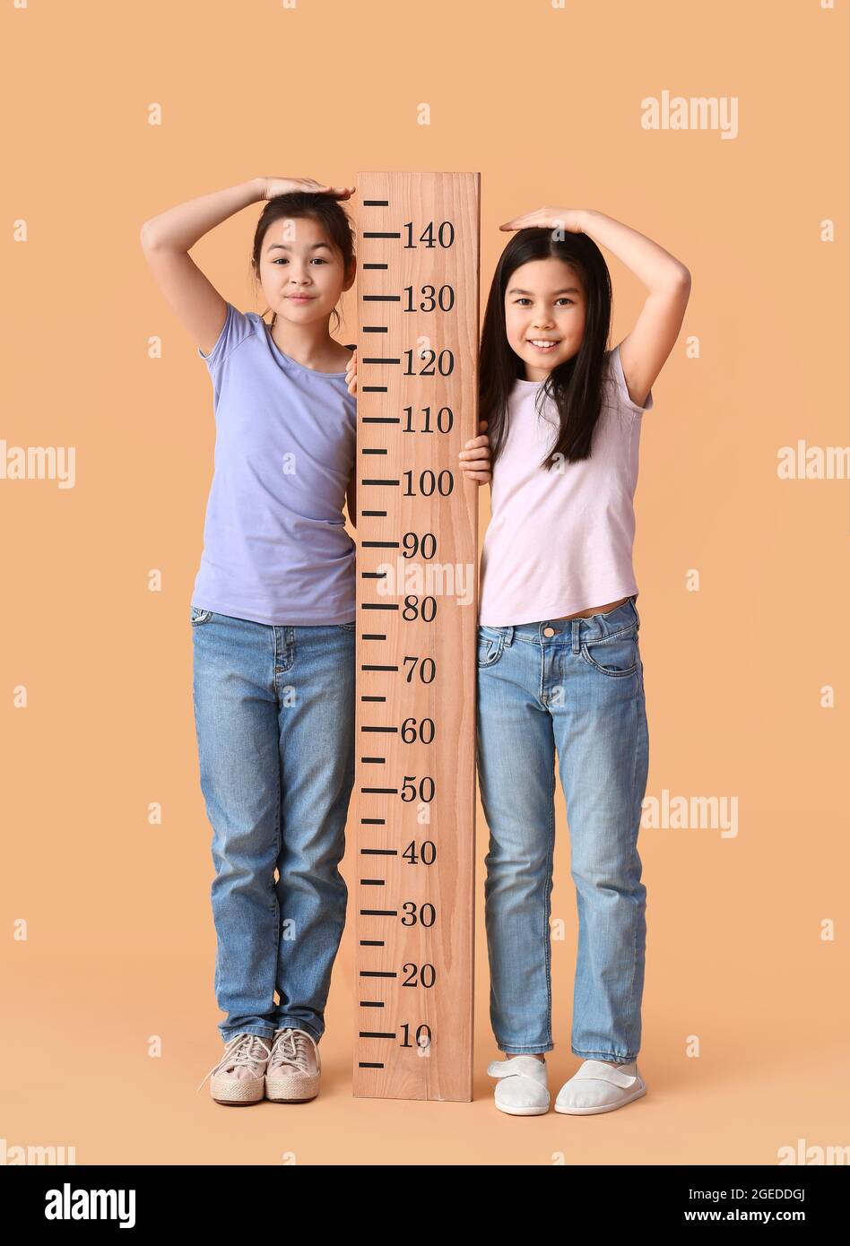 Cute little sisters measuring height on color background Stock