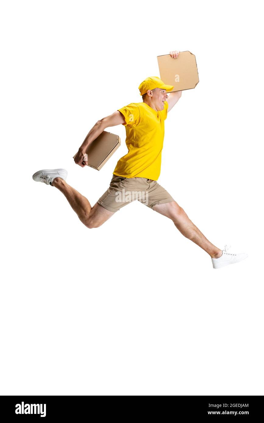 Young delivery man in yellow uniform running to deliver order isolated on white background. Concept of convenience, speed, comfort, safety, service. Stock Photo