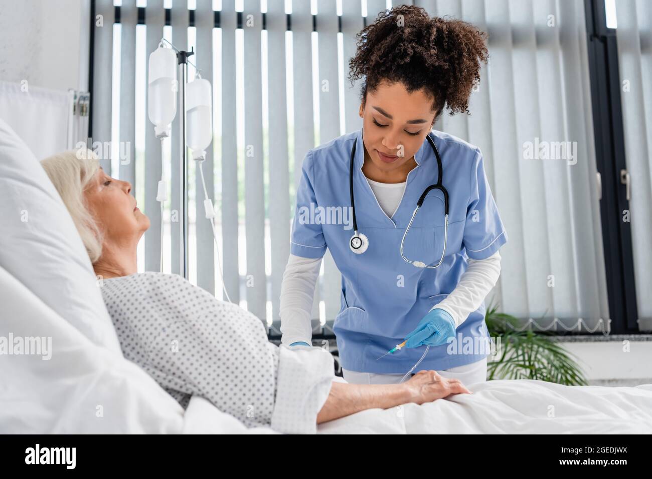 African american nurse holding catheter near elderly patient on bed in