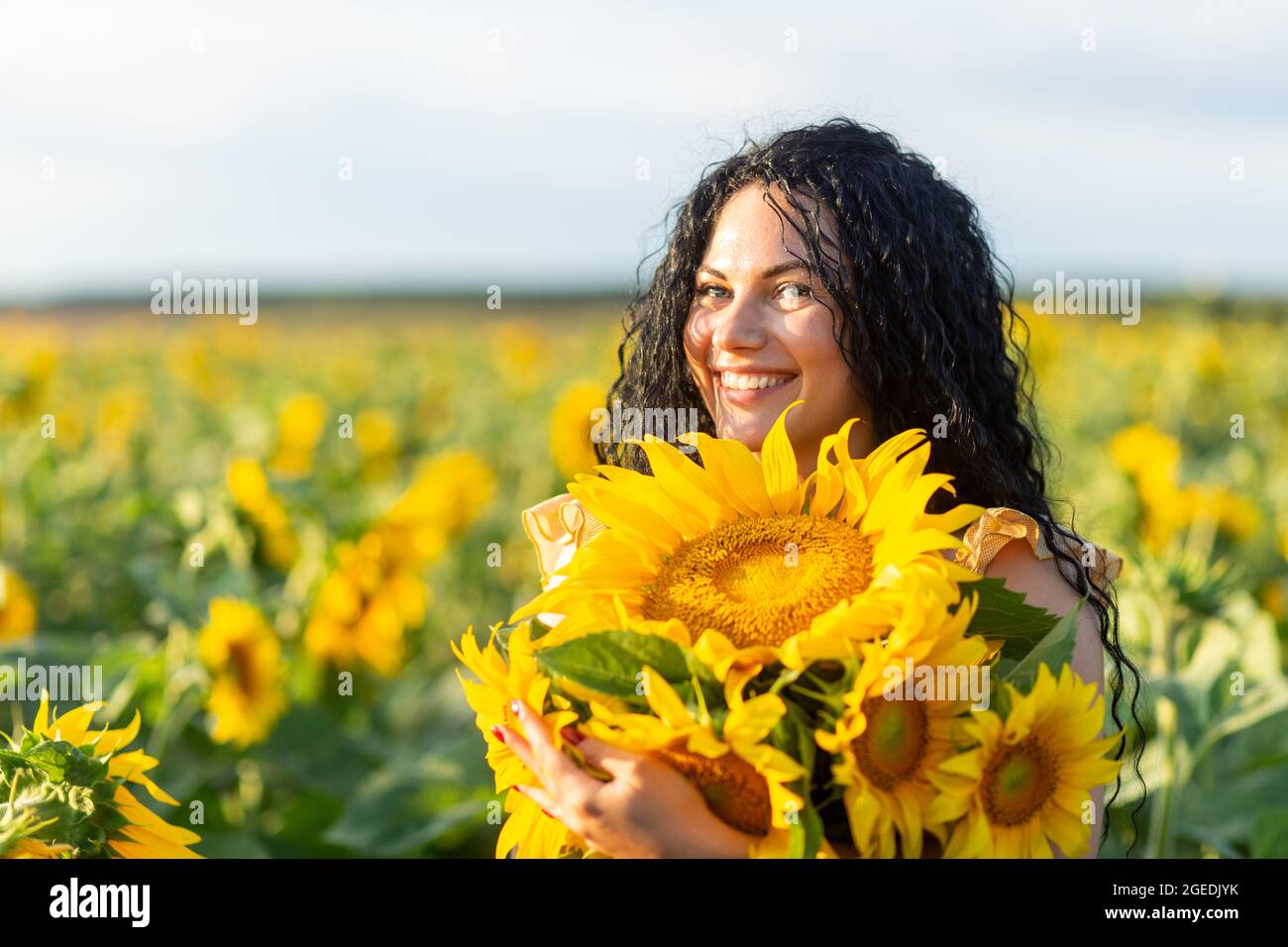 Portrait of a beautiful smiling dark-haired woman with bouquet of sunflowers Stock Photo