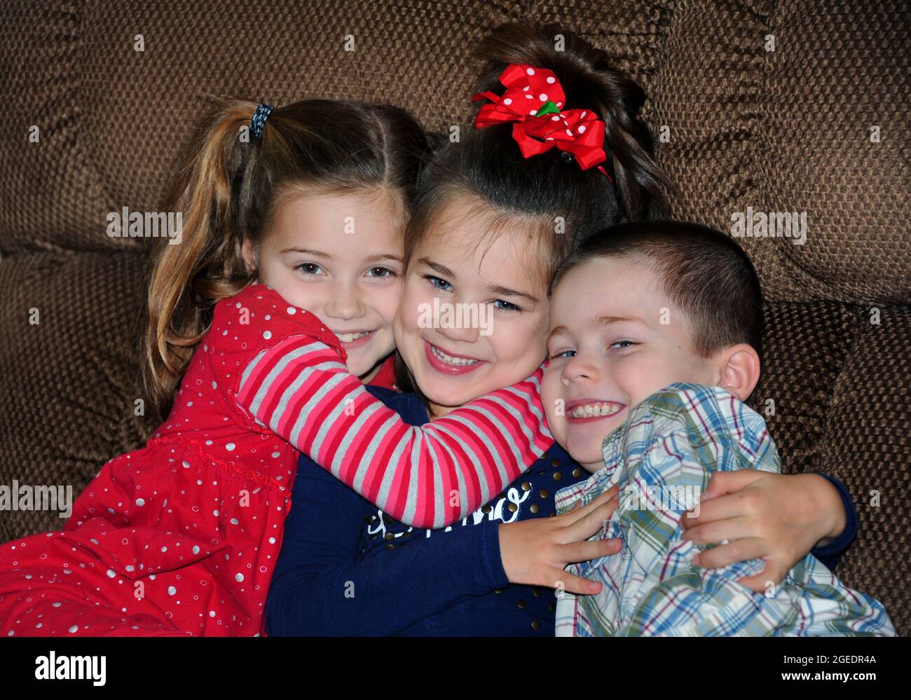 One brother and two sisters group hug on a sofa in their home.  They have huge grins on their face and beam happiness and love. Stock Photo