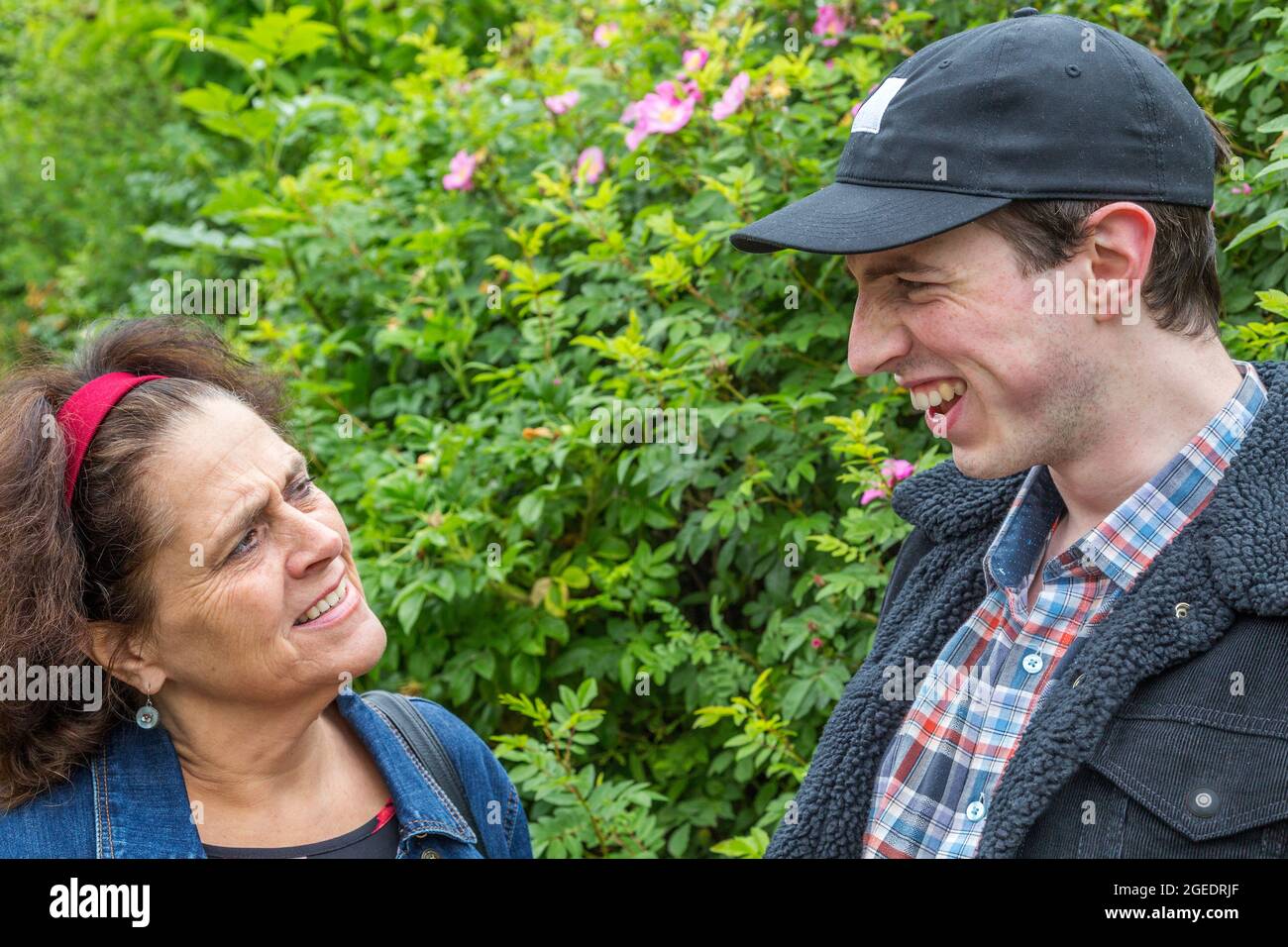 A middle aged woman looks confused as a yoinger man pulls a face and laughs. Stock Photo