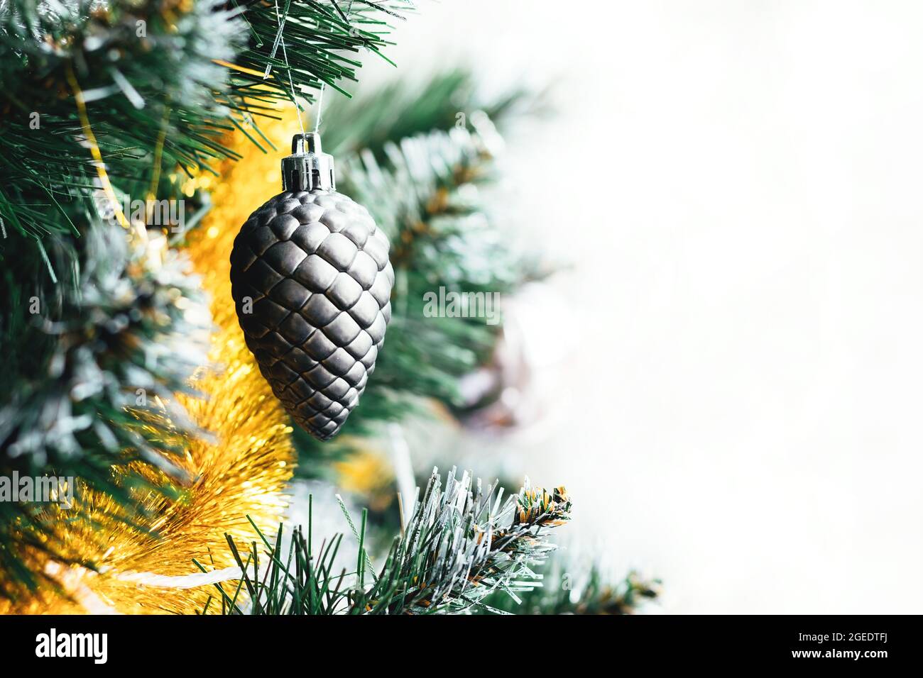 Silver gray toy cone hanging on Christmas tree with golden yellow tinsel garland on white background. Holiday banner with copy space. Selective focus Stock Photo