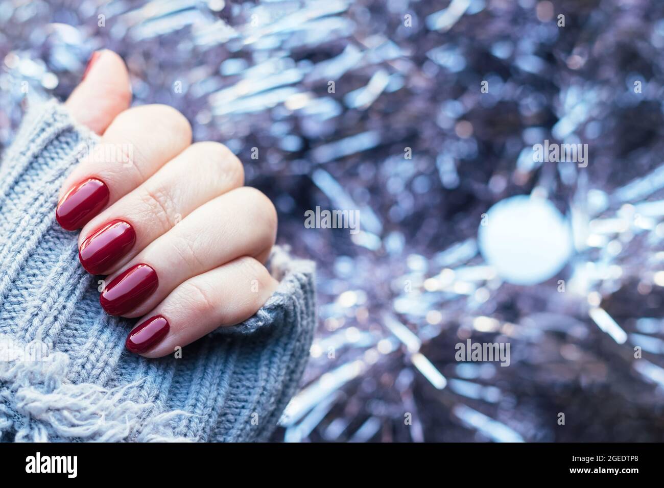 Female hand in a gray knitted sweater with a beautiful glossy manicure -  burgundy, dark red, cherry color nails on background of pale pink Christmas  t Stock Photo - Alamy