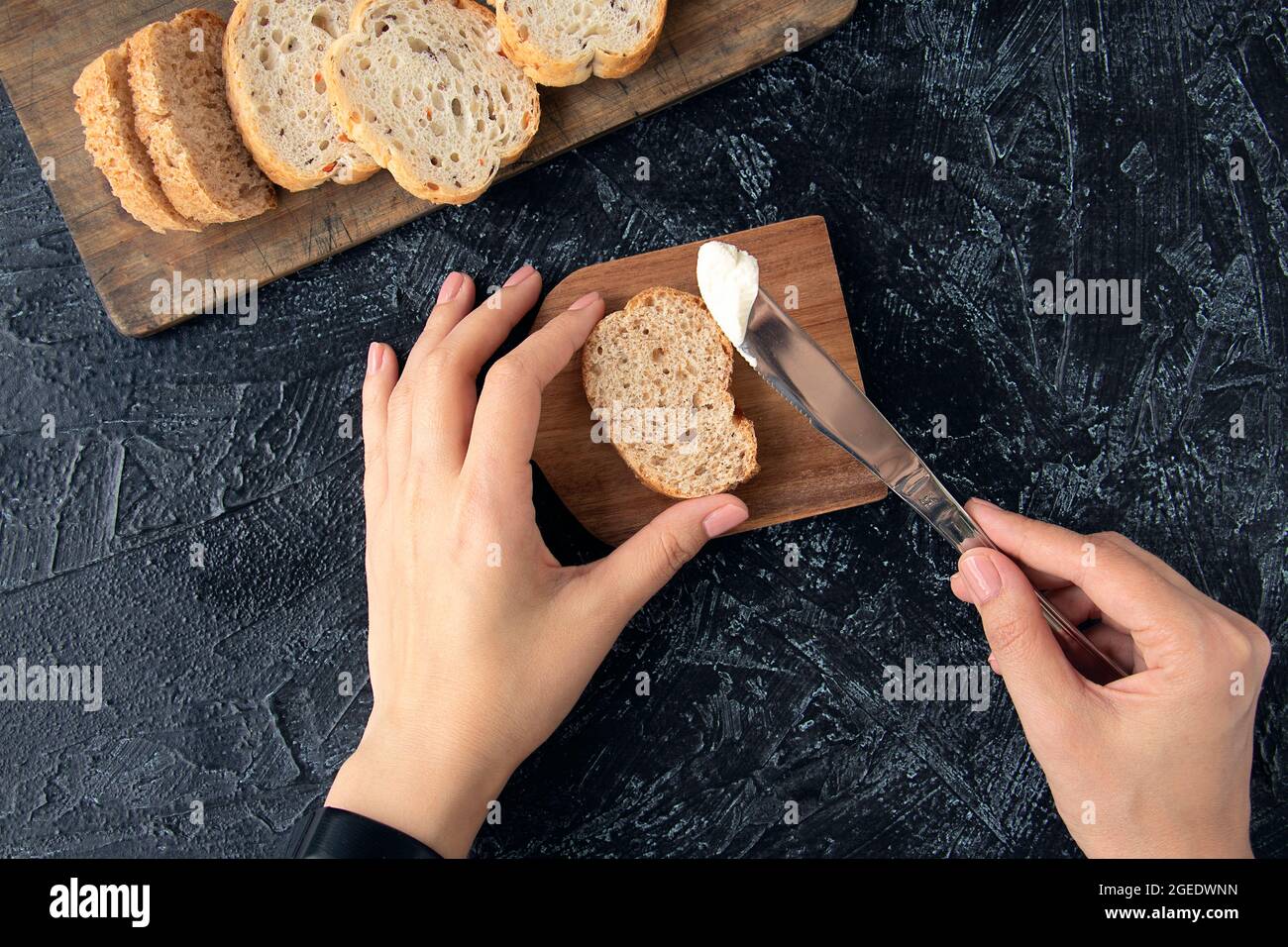female hands hold a knife with cream cheese and a piece of bread on a