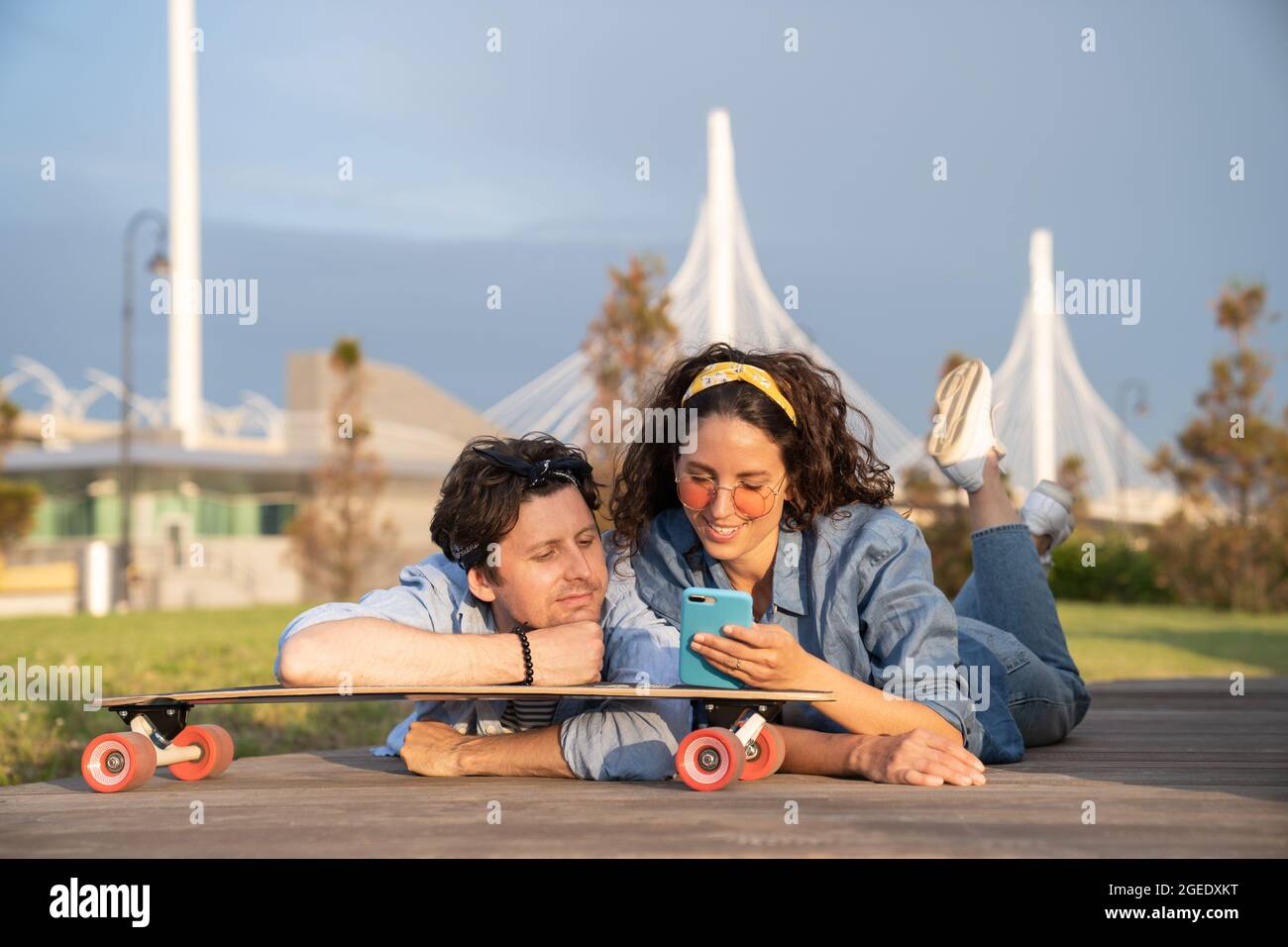 Trendy couple browsing web on smartphone outdoors using 4g internet connection lying on longboard Stock Photo