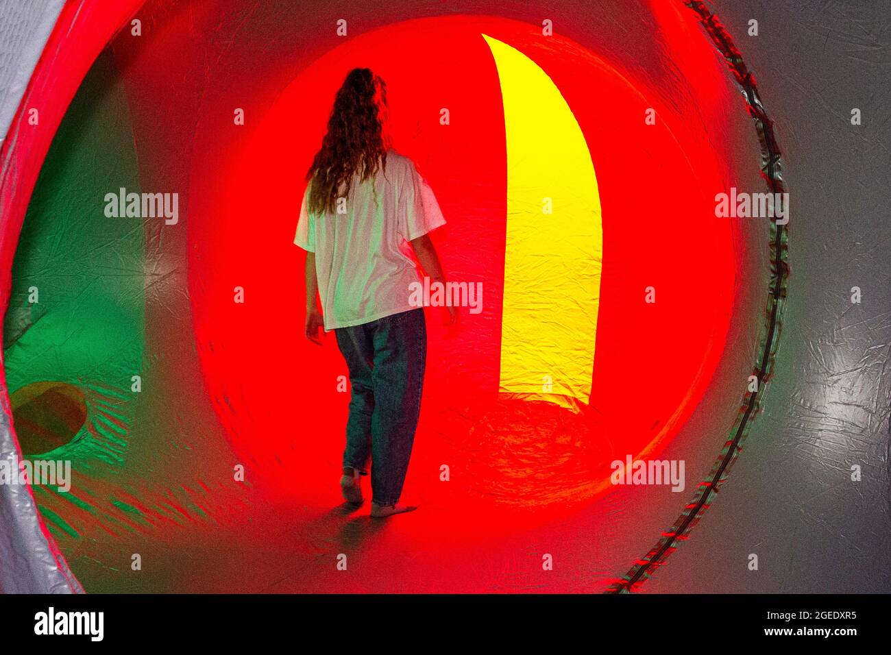 Blackburn, Lancashire, UK. 19th Aug 2021.  Zoe Felix explores the changing patterns of light, shifting as they pass through labyrinthine passages, Dodecalis Luminarium provides moments of pause in meditative stillness and quiet wonder in the furthest corners of the precision-engineered, ‘hide and seek’ illuminated colour tunnels of light architecture. Credit: MediaWorldImages/Alamy Live News Stock Photo