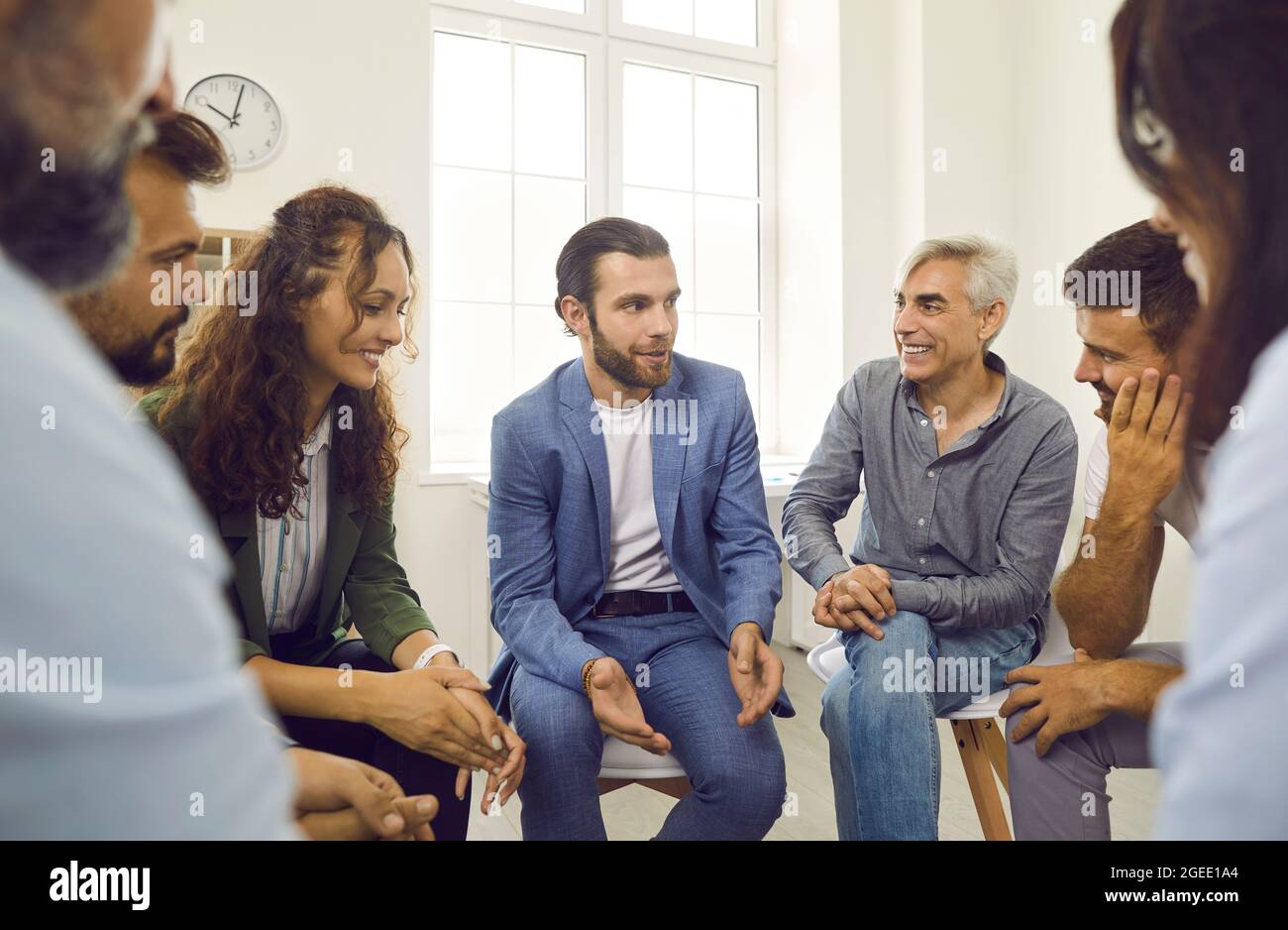 Young business coach or psychologist having a discussion with a happy group of people Stock Photo