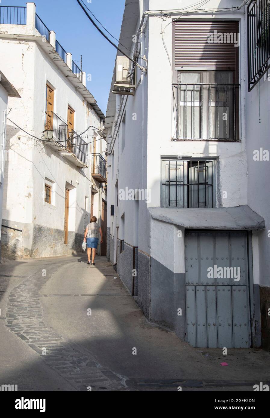 Laroles of the Alpujarras street with a small blue door in front and in the background a woman walking Stock Photo