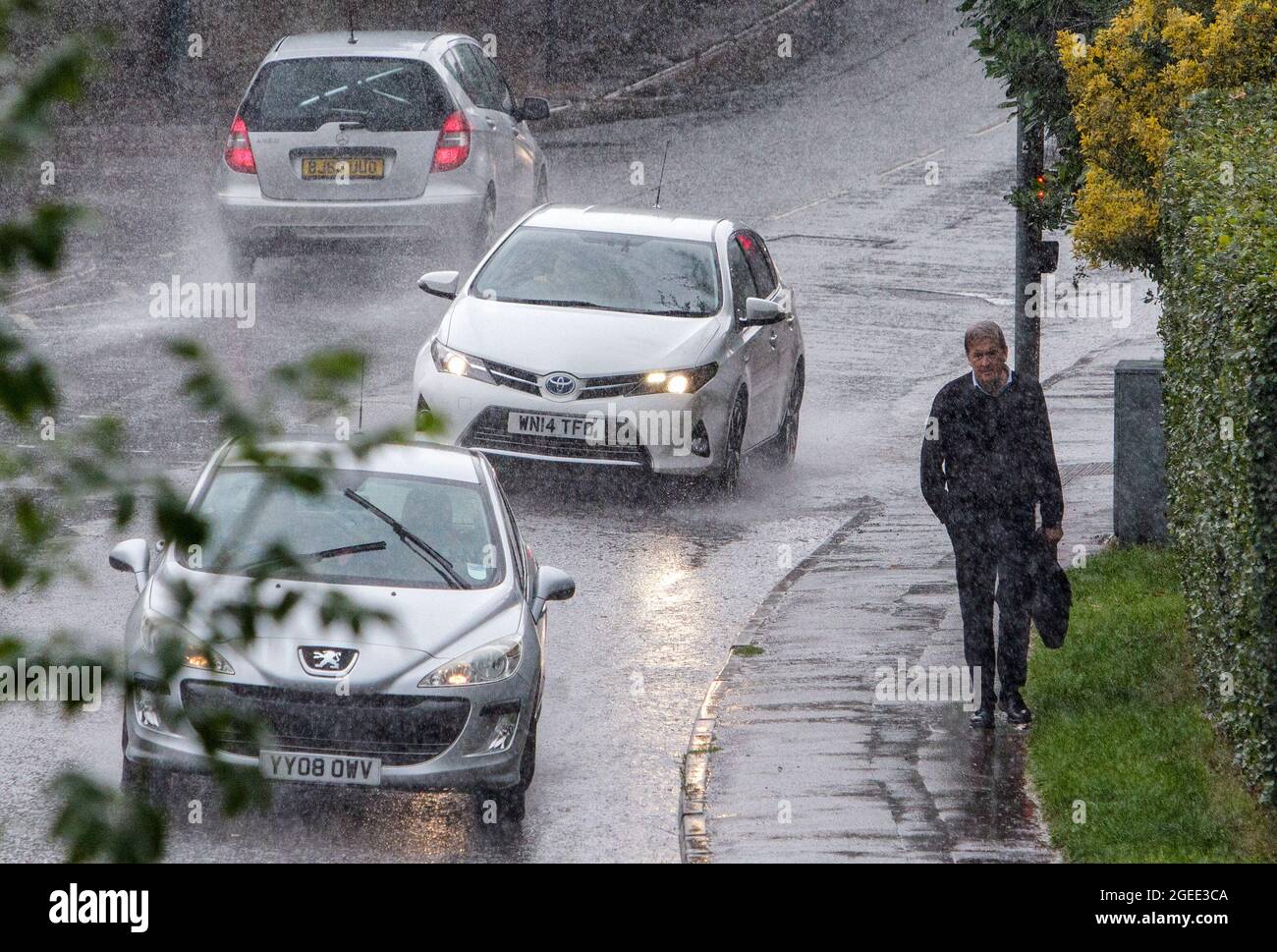 Chippenham, Wiltshire, UK. 19th August, 2021. Drivers and a pedestrian are pictured braving heavy rain in Chippenham as torrential rain showers make their way across the UK. Credit: Lynchpics/Alamy Live News Stock Photo