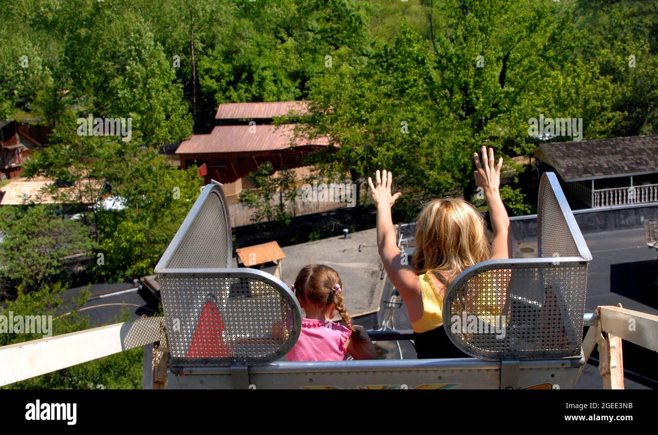 Mother and little daughter experience a first time on a Ferris Wheel.  Daughter hangs on and Mom raises her hands as they get to the top on a Ferris W Stock Photo