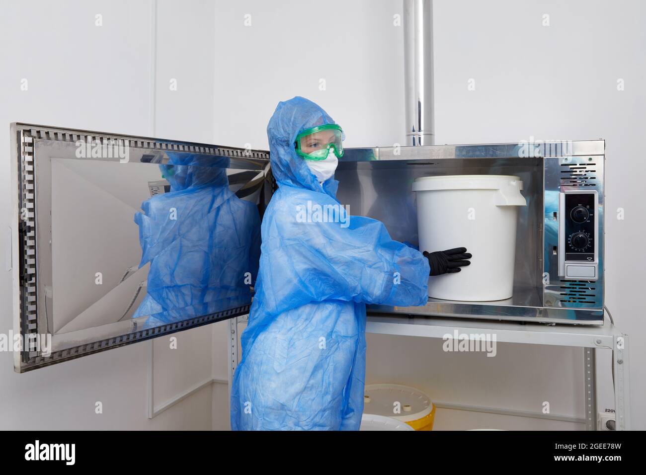 Technologist wearing PPE protective suit, mask, gloves working with big plastic bucket in research laboratory Stock Photo