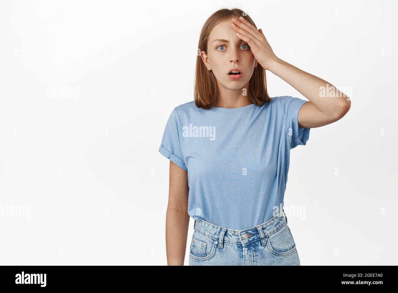 Shocked and confused girl hold hand on head and stare puzzled at camera, forgot remember smth important, cant understand what happened, standing Stock Photo