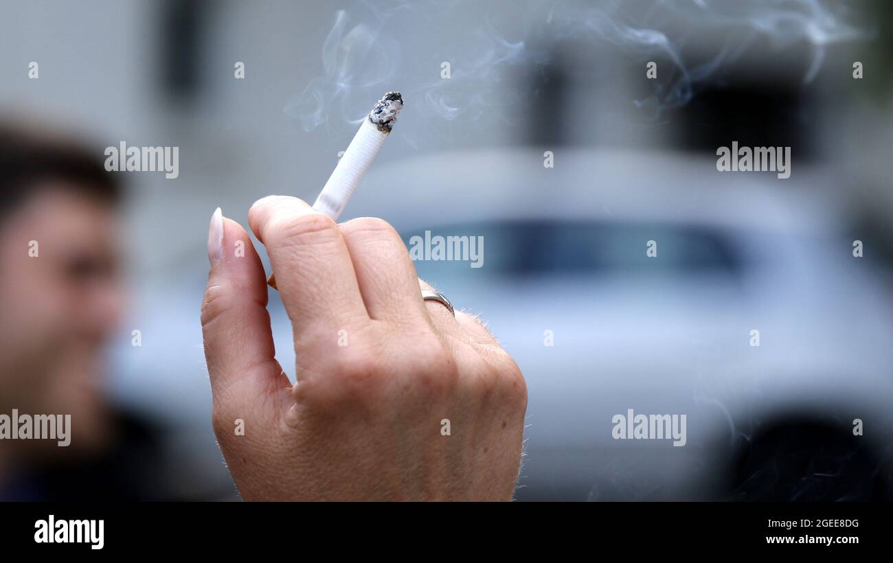 Closeup of a woman's hand holding a half-smoked cigarette on a blurry  background Stock Photo