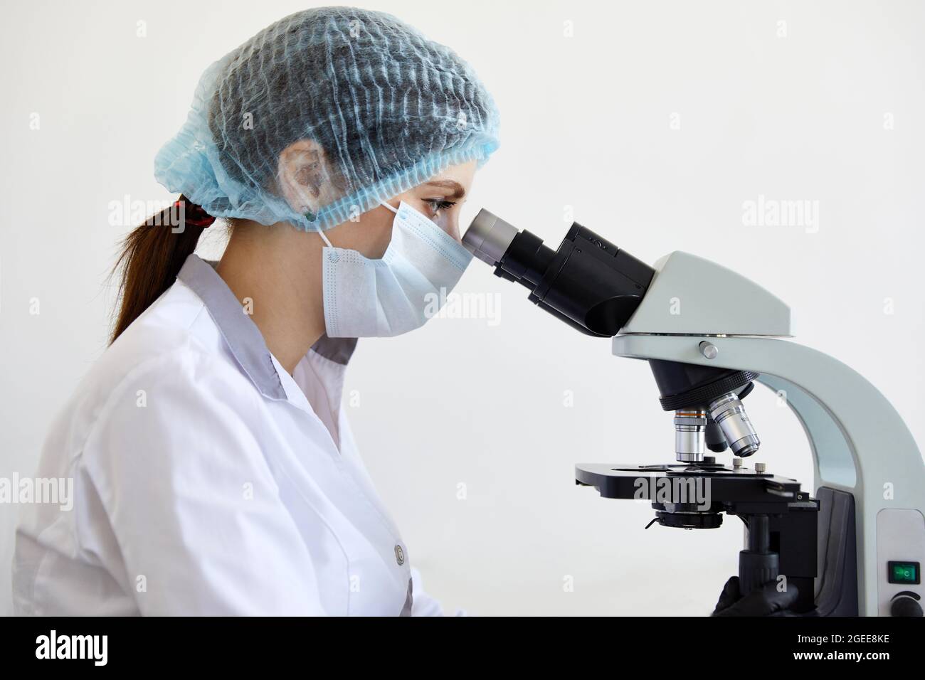 Female scientist looking through microscope in modern chemical laboratory doing some research. Analyzing samples using a microscope Stock Photo