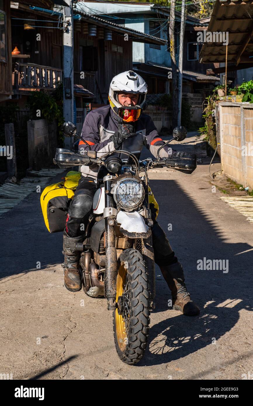 man stopping on road with his motorcycle in Thai village Stock Photo