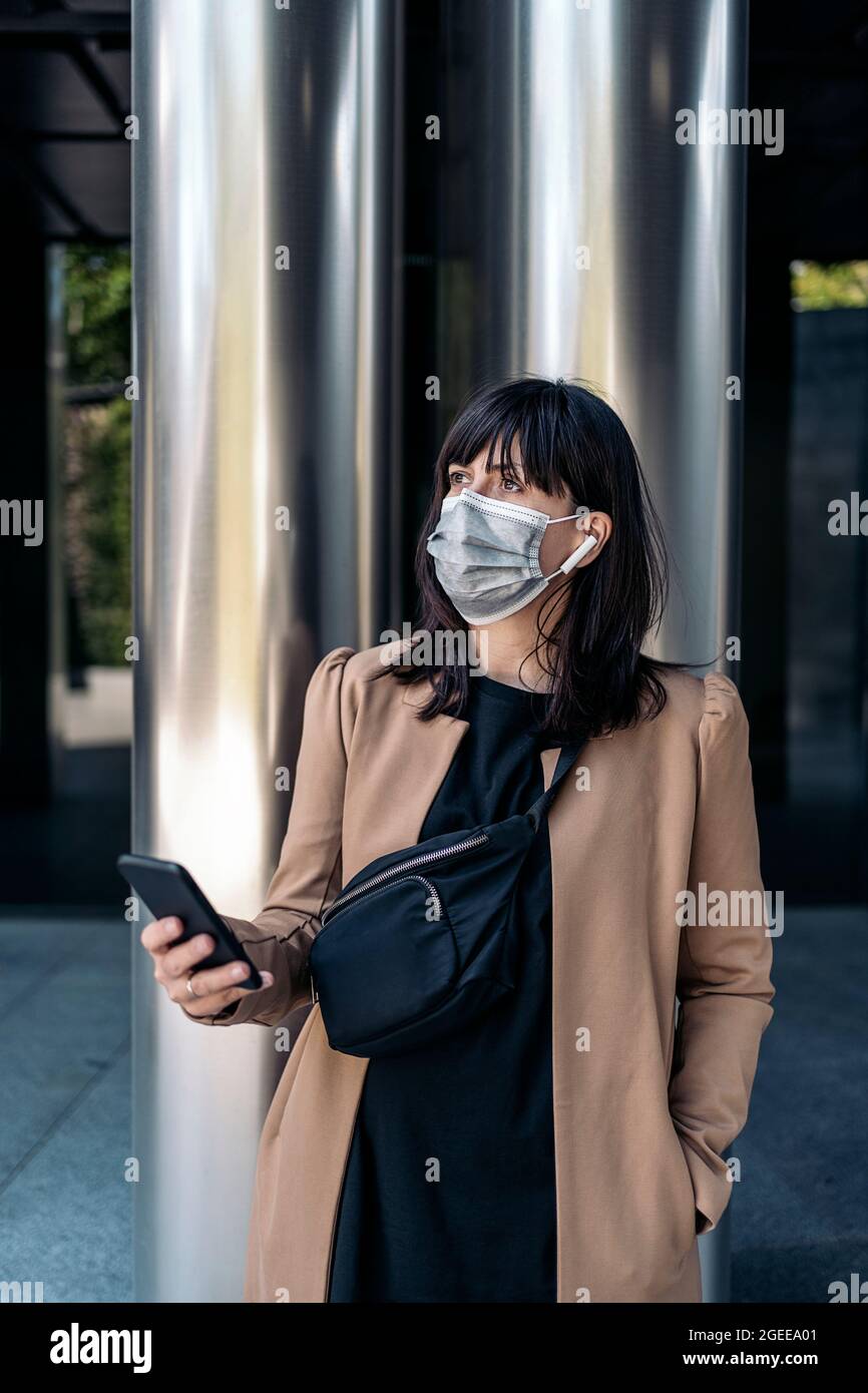 Caucasian businesswoman talking on the phone outdoors wearing a face mask Stock Photo