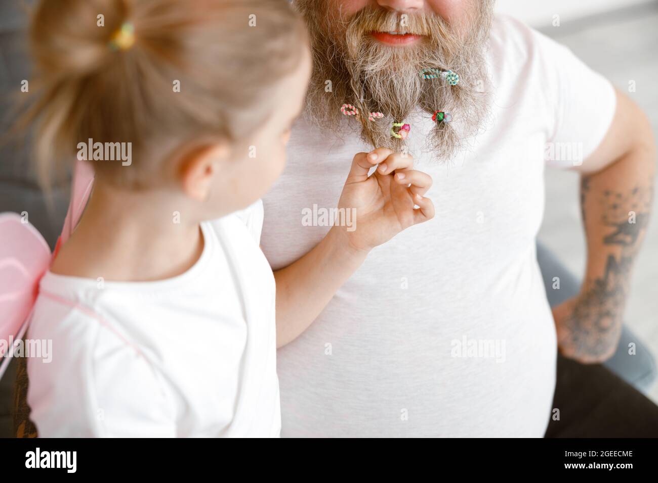 Curious little girl touches daddy beard with colorful scrunchies playing together at home Stock Photo