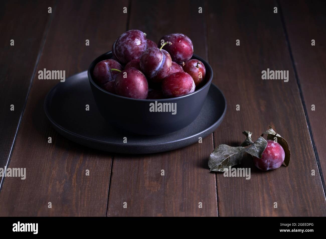 Fresh ripe plums in a dish on table from natural dark wooden boards Stock Photo
