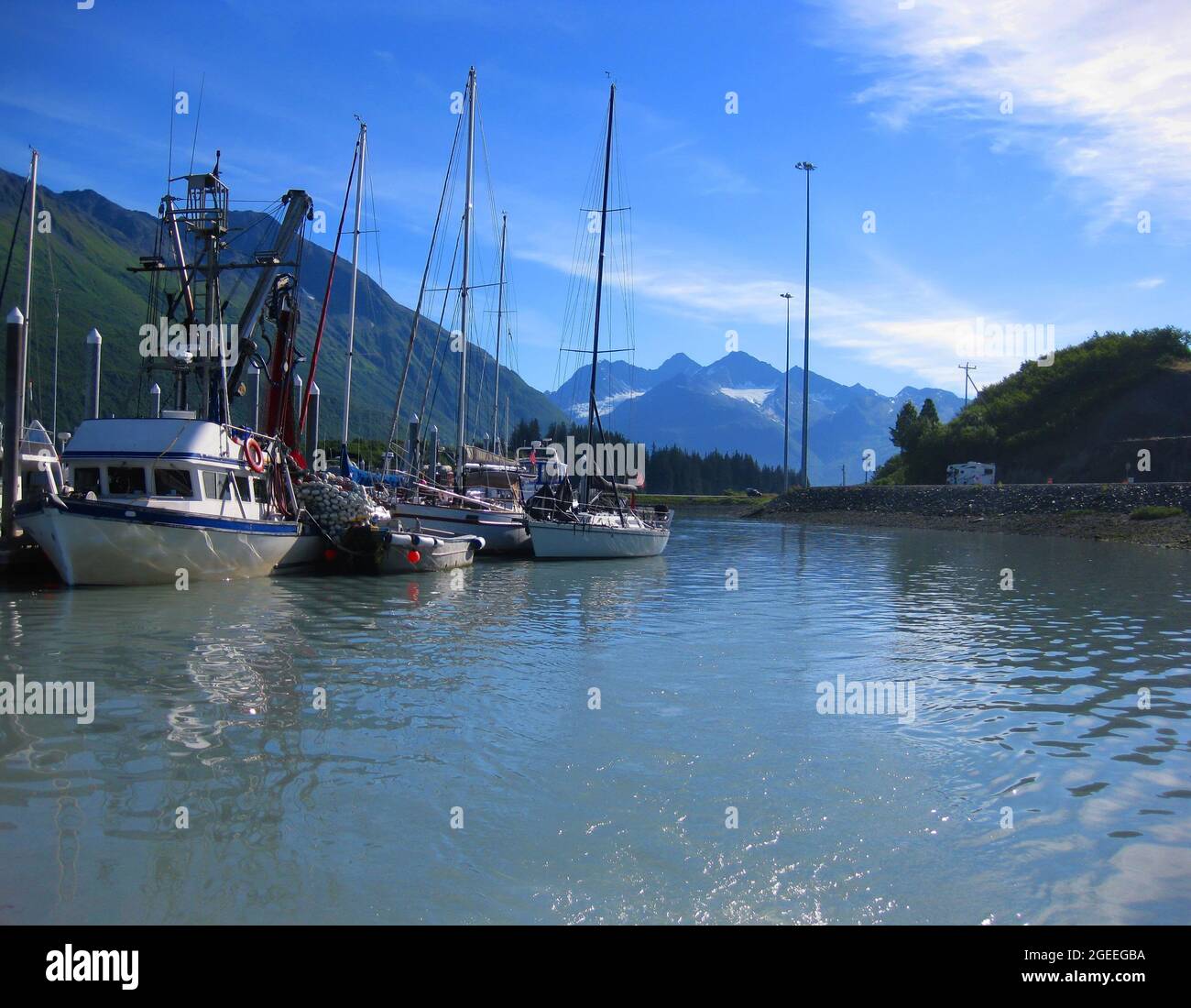 Beautiful mountains tower over the small boat harbor in Valdez, Alaska.  Sailboats and fishing boats cluster together. Stock Photo