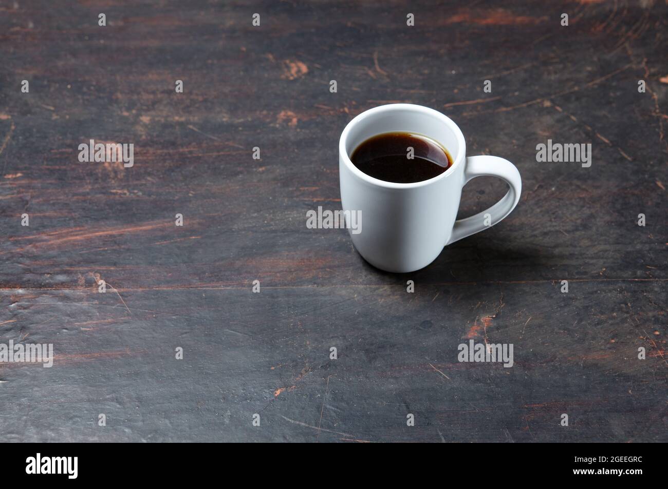 White cup with coffee on a dark wooden background, closeup. Tasty breakfast, morning routine concept Stock Photo
