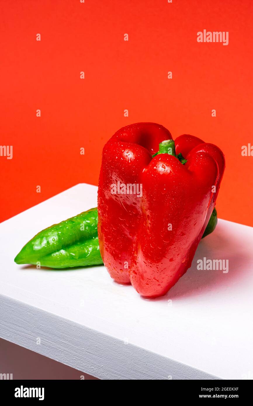 Photograph of a red pepper and a green Italian pepper on a white wood and red background.The photo is shot from a top point of view and in vertical fo Stock Photo