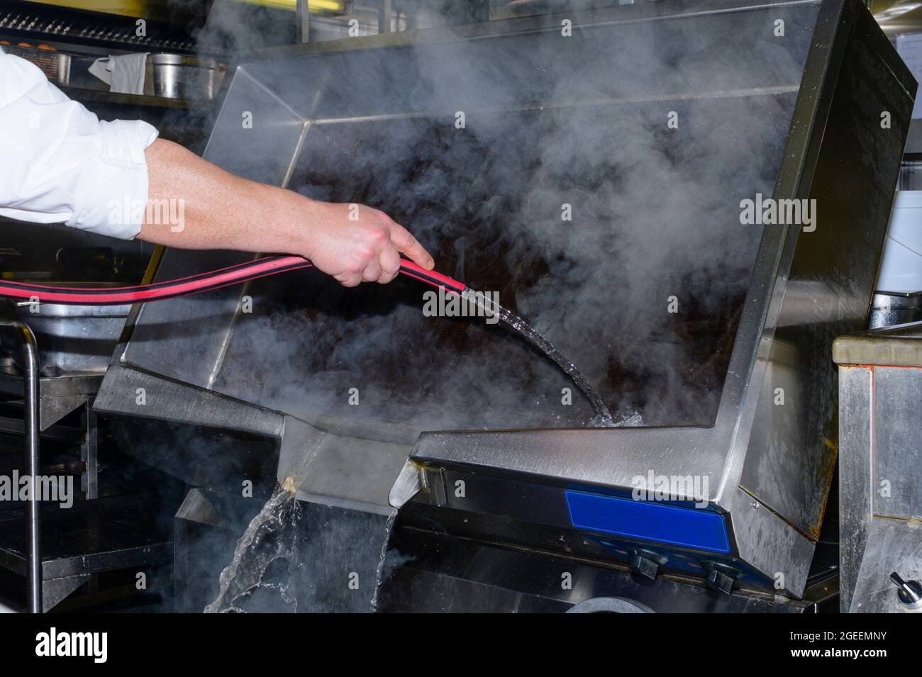 A cook cleans the large electric pan with hose and water Stock Photo