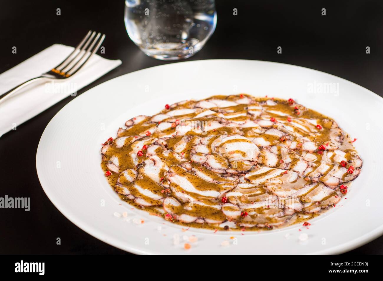 Octopus Carpaccio. Seafood raw octopus slices with olive oil and black pepper on a white plate. Stock Photo