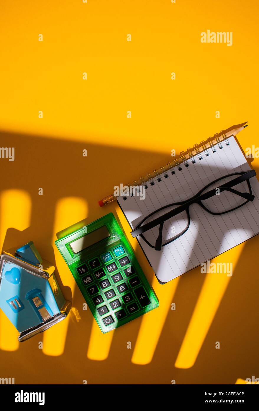 Vertical top view of a vibrant orange shadowy table with stationery on it next to a blue house toy Stock Photo