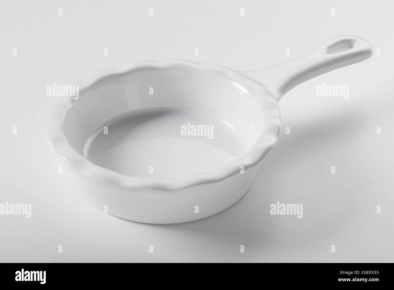 New round white ceramic baking bowl with a handle and wavy edges on